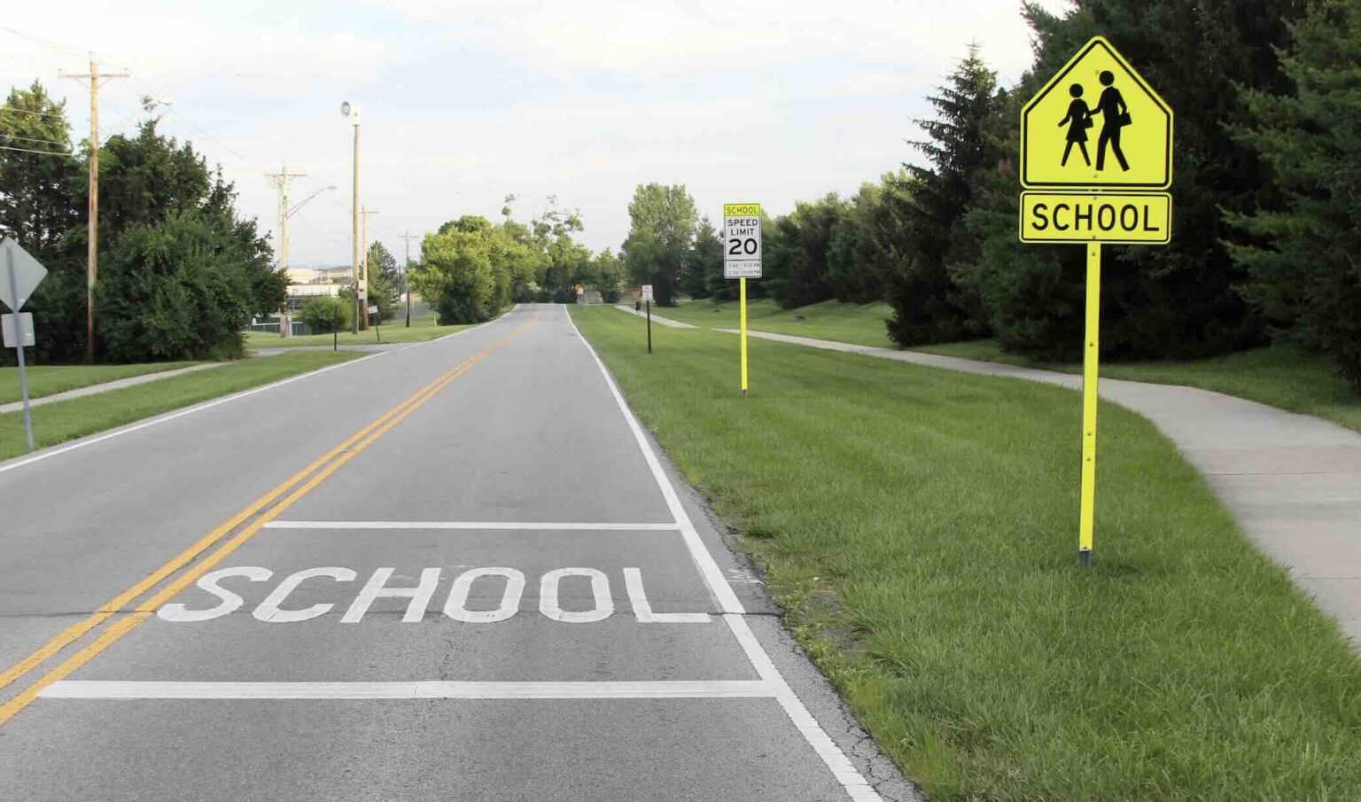 Road entering an active school zone showing pavement markings, school crossing signs, and a posted speed limit | Daniel Stark Injury Lawyers