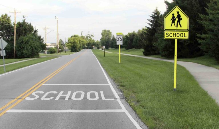 Road entering an active school zone showing pavement markings, school crossing signs, and a posted speed limit | Daniel Stark Injury Lawyers