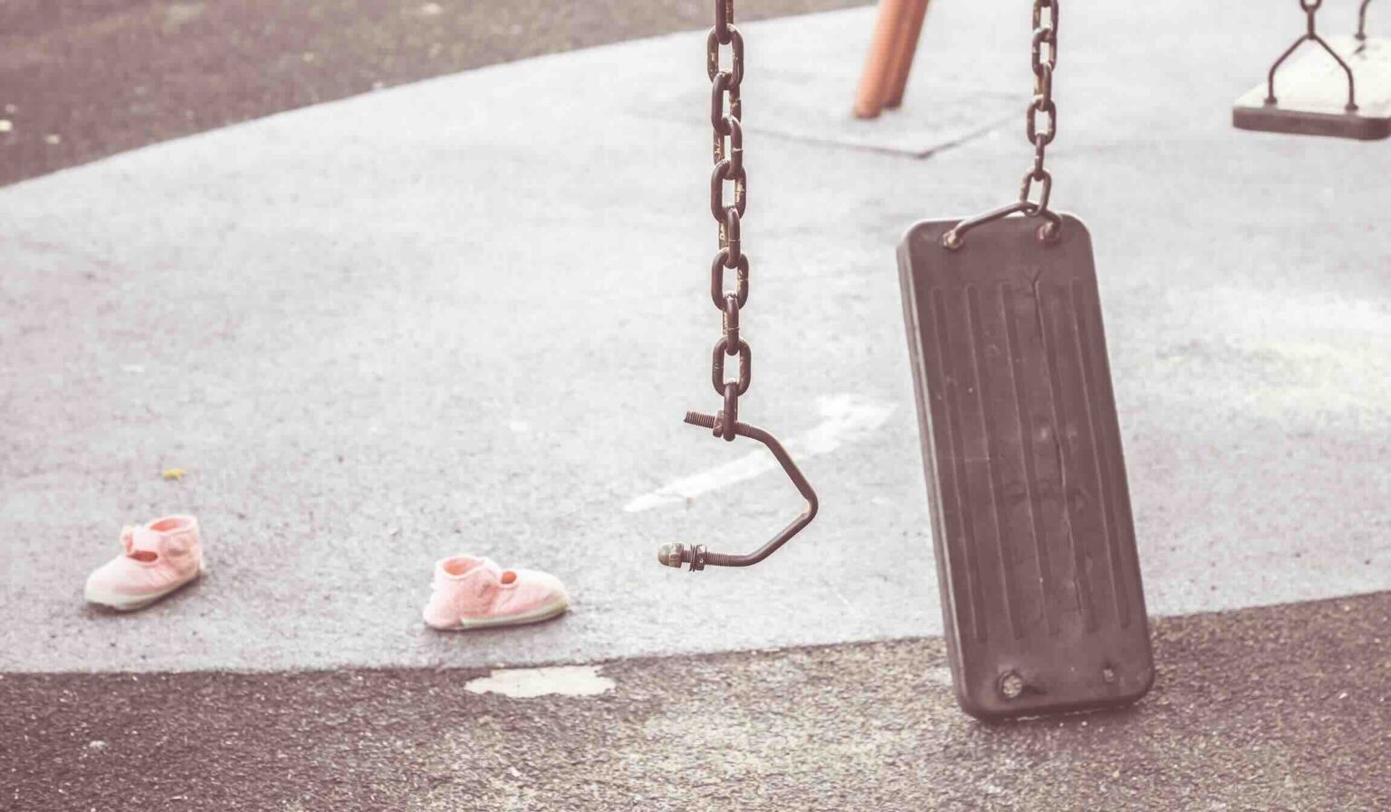 Pink toddler shoes on the ground next to broken swing representing playground injury | Daniel Stark Injury Lawyers