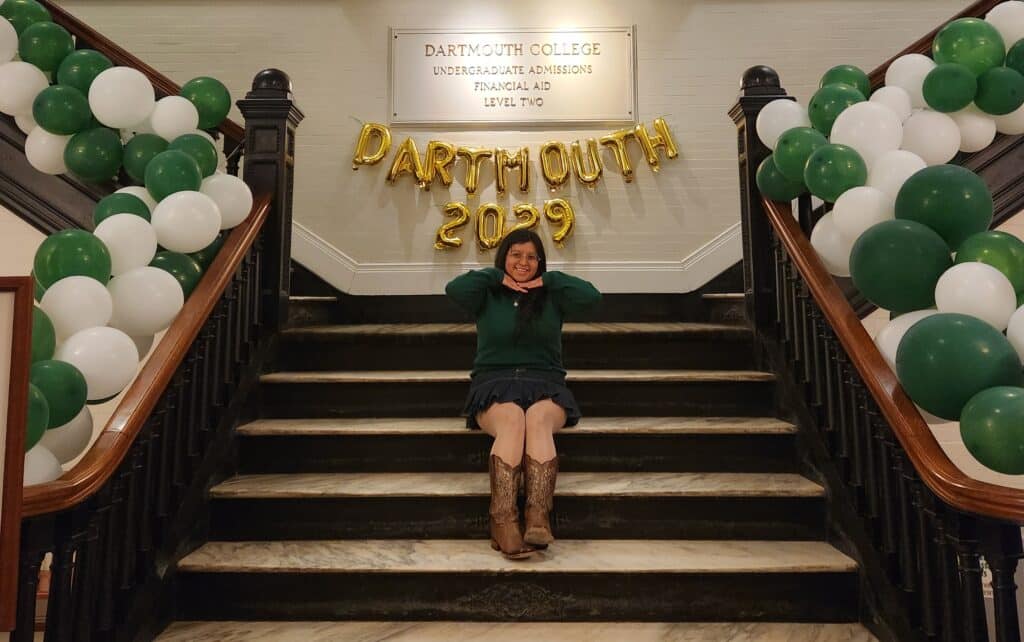 A girl posing and smiling on a staircase under a series of balloon letters in gold text reading 'DARTMOUTH 2029' | Daniel Stark Law