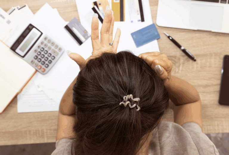 Back view of woman struggling with money management, bills and credit cards spread across desk | Daniel Stark Law