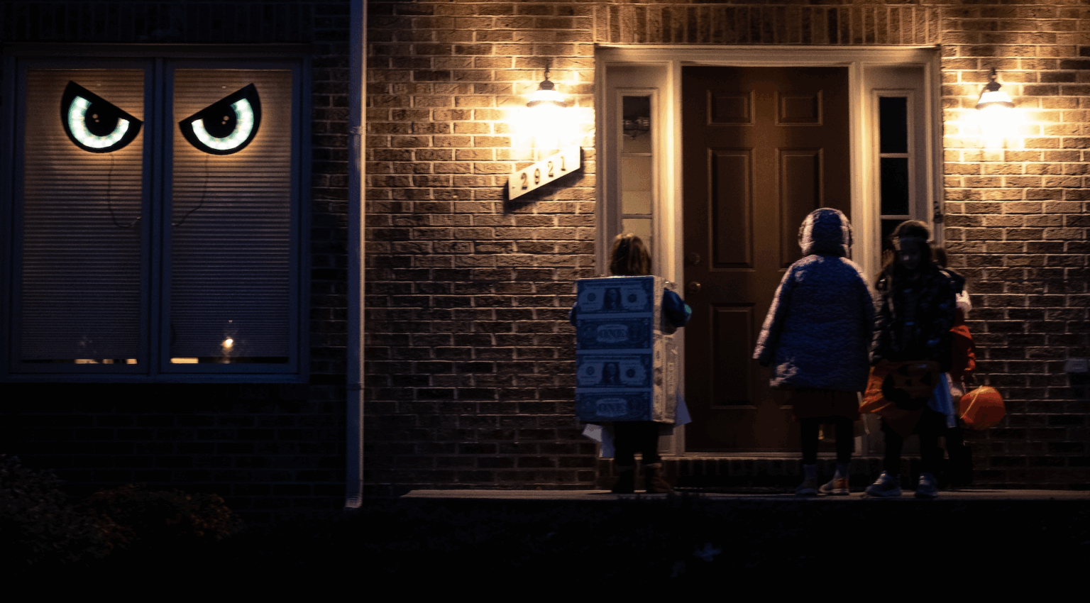 Children dressed in Halloween costumes at a closed door illuminated by porch lights | Daniel Stark Injury Lawyers