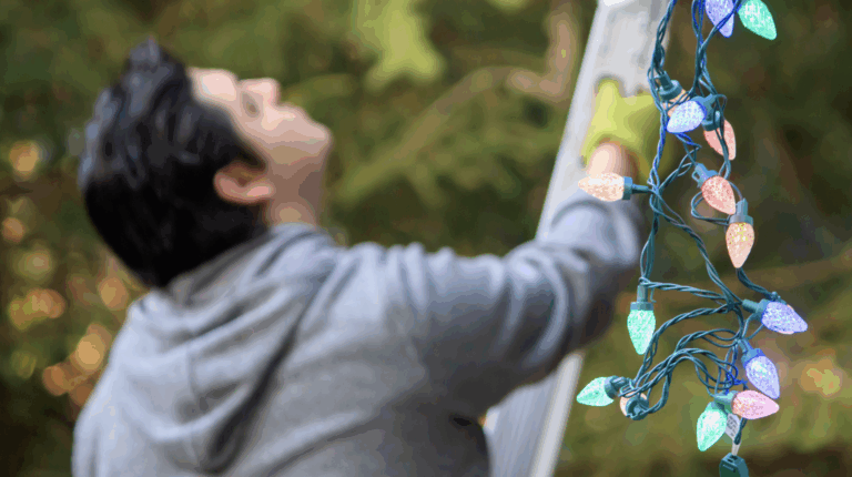 Man in grey jacket with gloves setting up ladder to hang Christmas lights professionally | Daniel Stark Injury Lawyers