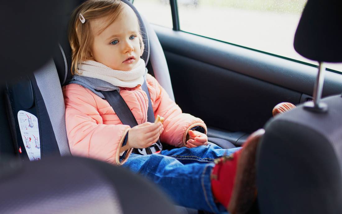 Toddler in a pink winter jacket secured in a five-point harness car seat inside a family vehicle | Daniel Stark Injury Lawyers