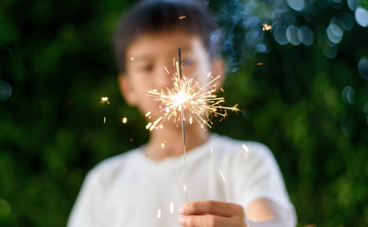 Blurred image of a young boy holding a burning sparkler, with the bright sparkler flame in focus during a fireworks celebration | Daniel Stark Injury Lawyers