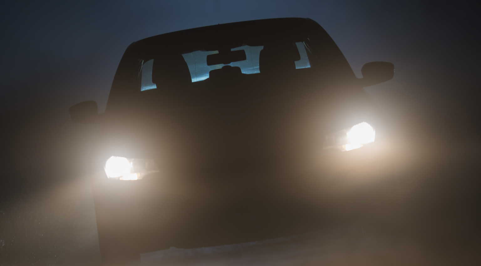 Car driving through fog at night with headlights on for visibility | Daniel Stark Injury Lawyers