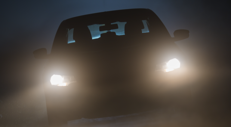 Car driving through fog at night with headlights on for visibility | Daniel Stark Injury Lawyers