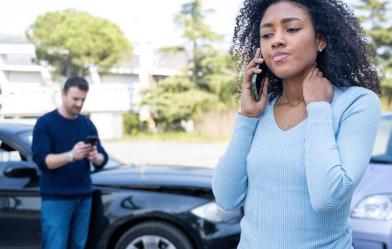 Woman on the phone after a car accident with vehicles blurred in the background | Daniel Stark Injury Lawyers