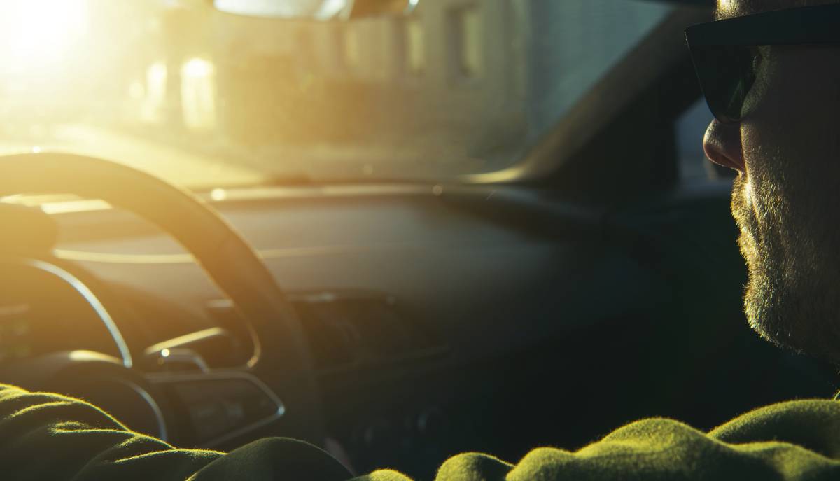 Man driving a car while wearing sunglasses as bright sunlight glares through the windshield | Daniel Stark Injury Lawyers