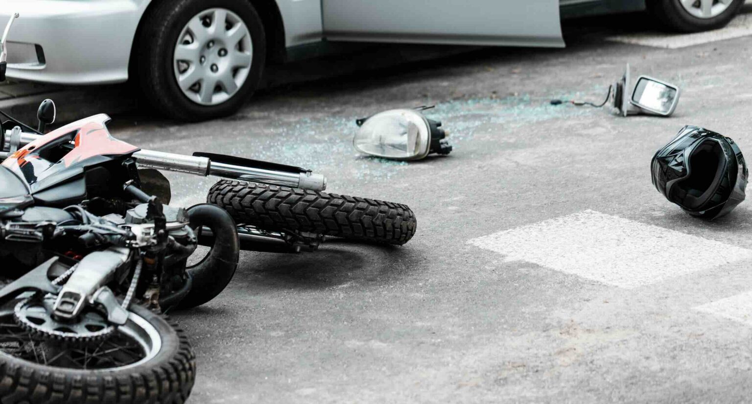 Motorcycle on its side in the roadway with debris, broken glass, and a helmet after a car accident | Daniel Stark Injury Lawyers