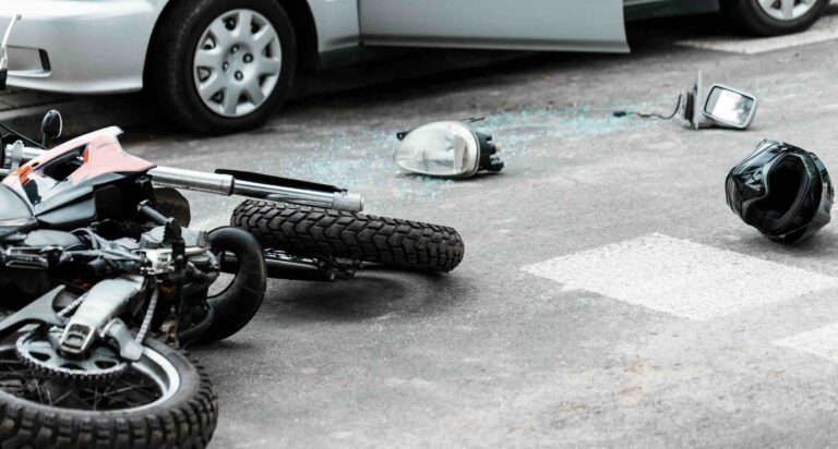 Motorcycle on its side in the roadway with debris, broken glass, and a helmet after a car accident | Daniel Stark Injury Lawyers