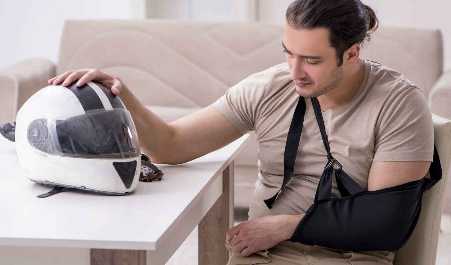 Motorcycle crash victim with arm injury sitting at table beside helmet, recovering from accident | Daniel Stark Injury Lawyers