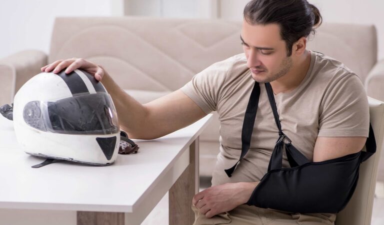 Motorcycle crash victim with arm injury sitting at table beside helmet, recovering from accident | Daniel Stark Injury Lawyers