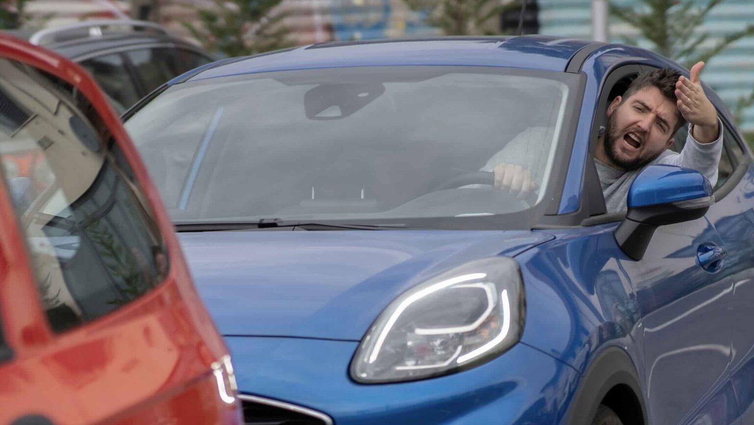 Man hanging out the window of a blue car shouting at the driver of a red car during a road rage incident, illustrating aggressive driving that could lead to civil liability | Daniel Stark Injury Lawyers